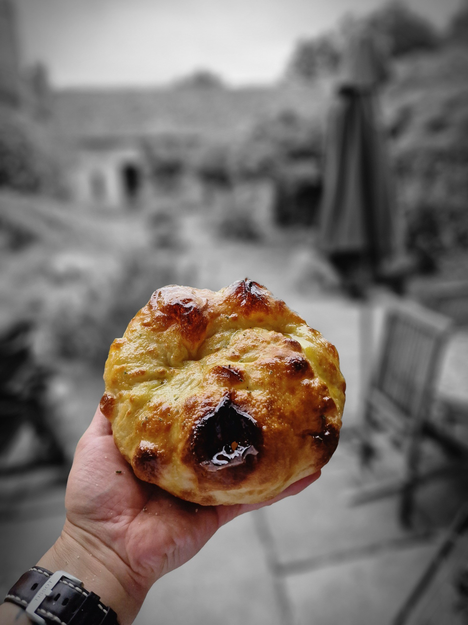 A hand holding a golden-brown baked pastry outdoors