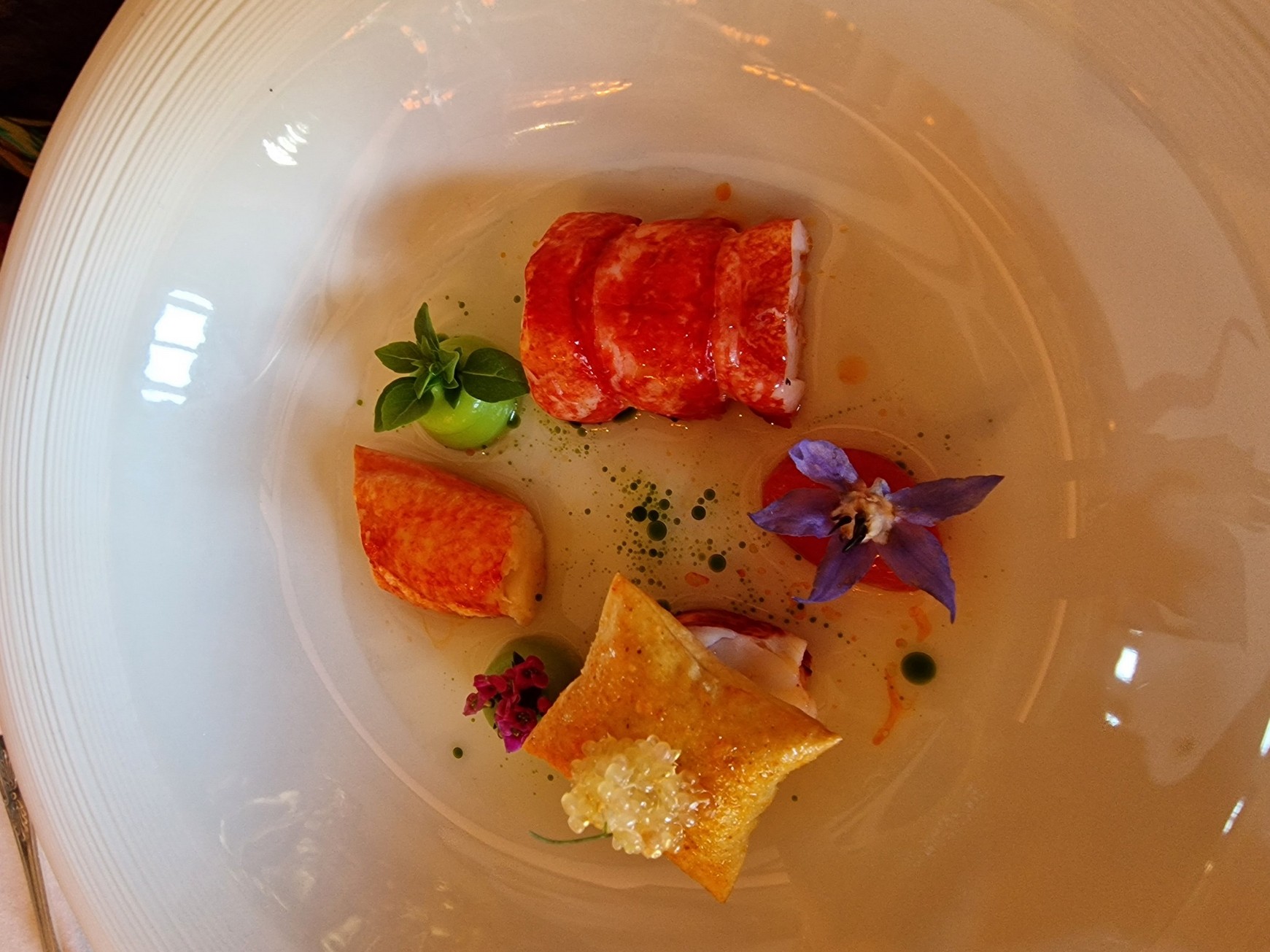 Butter-poached lobster with basil purée, filo crisp and borage flower in a white bowl