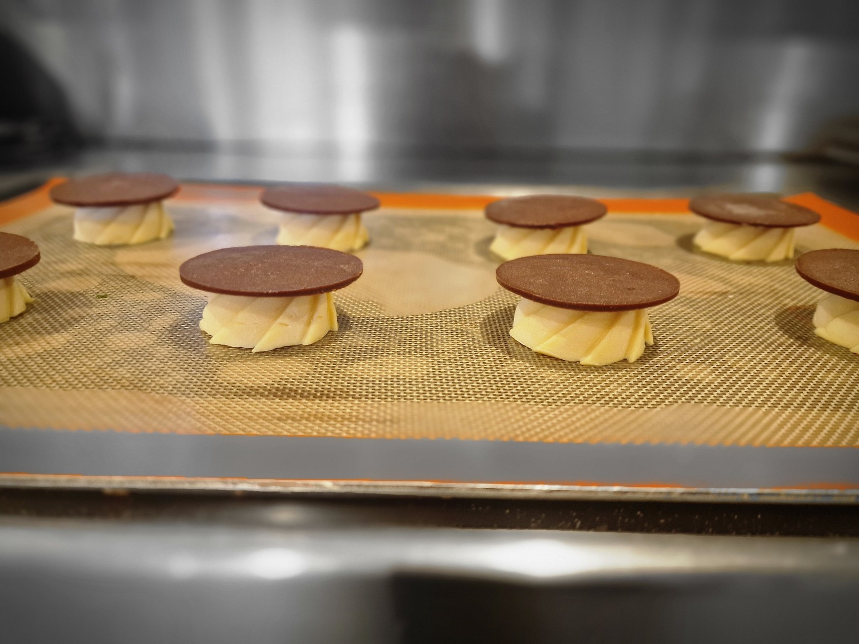 Tray of piped choux buns topped with craquelin discs before baking