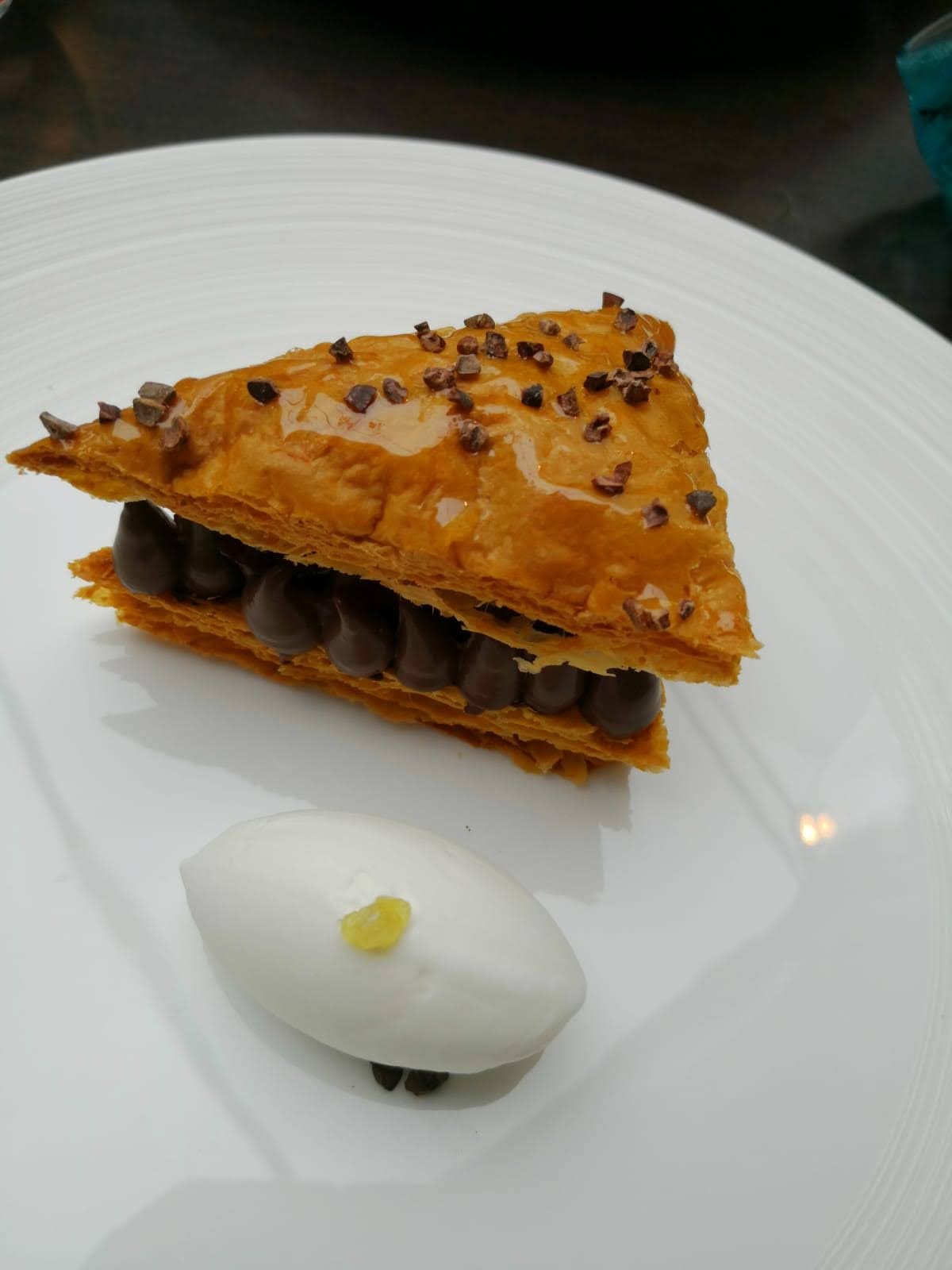 Triangular chocolate cream pastry with cocoa nibs and a scoop of white cream