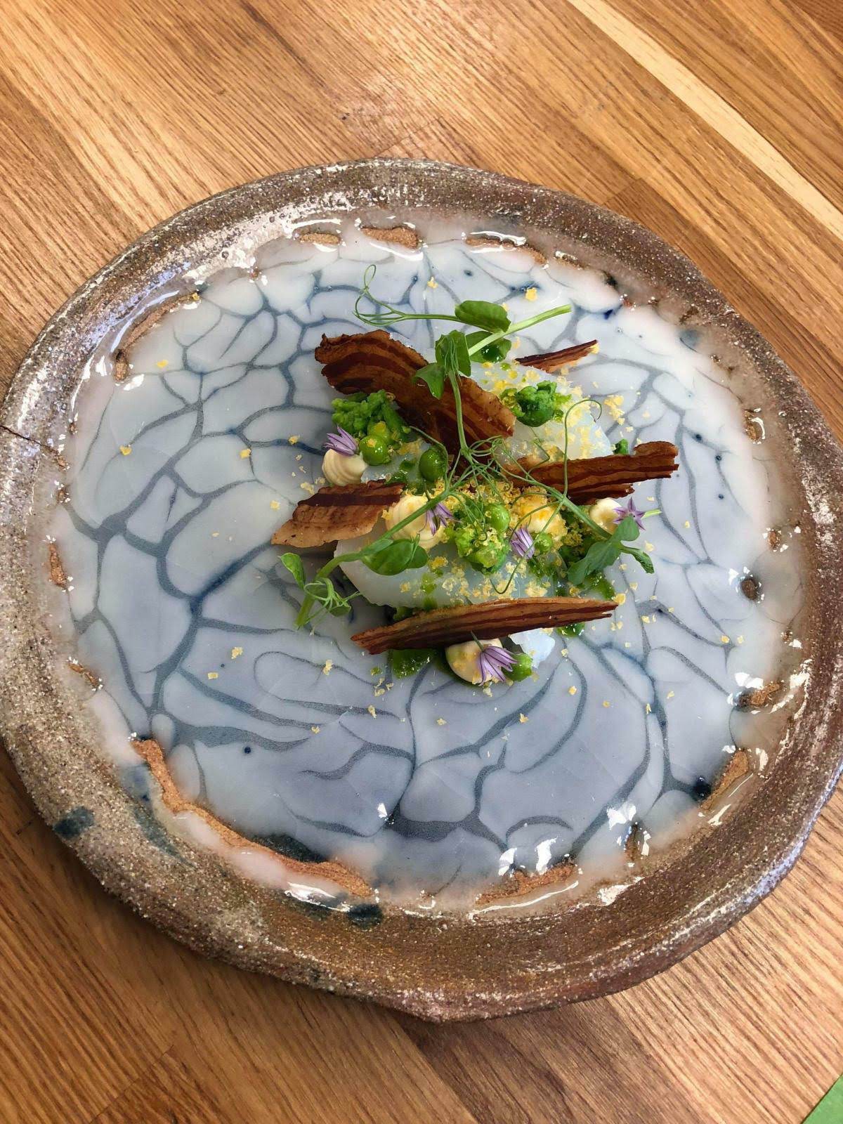 Poached cod with peas, chive flowers and cured pork on a ceramic plate