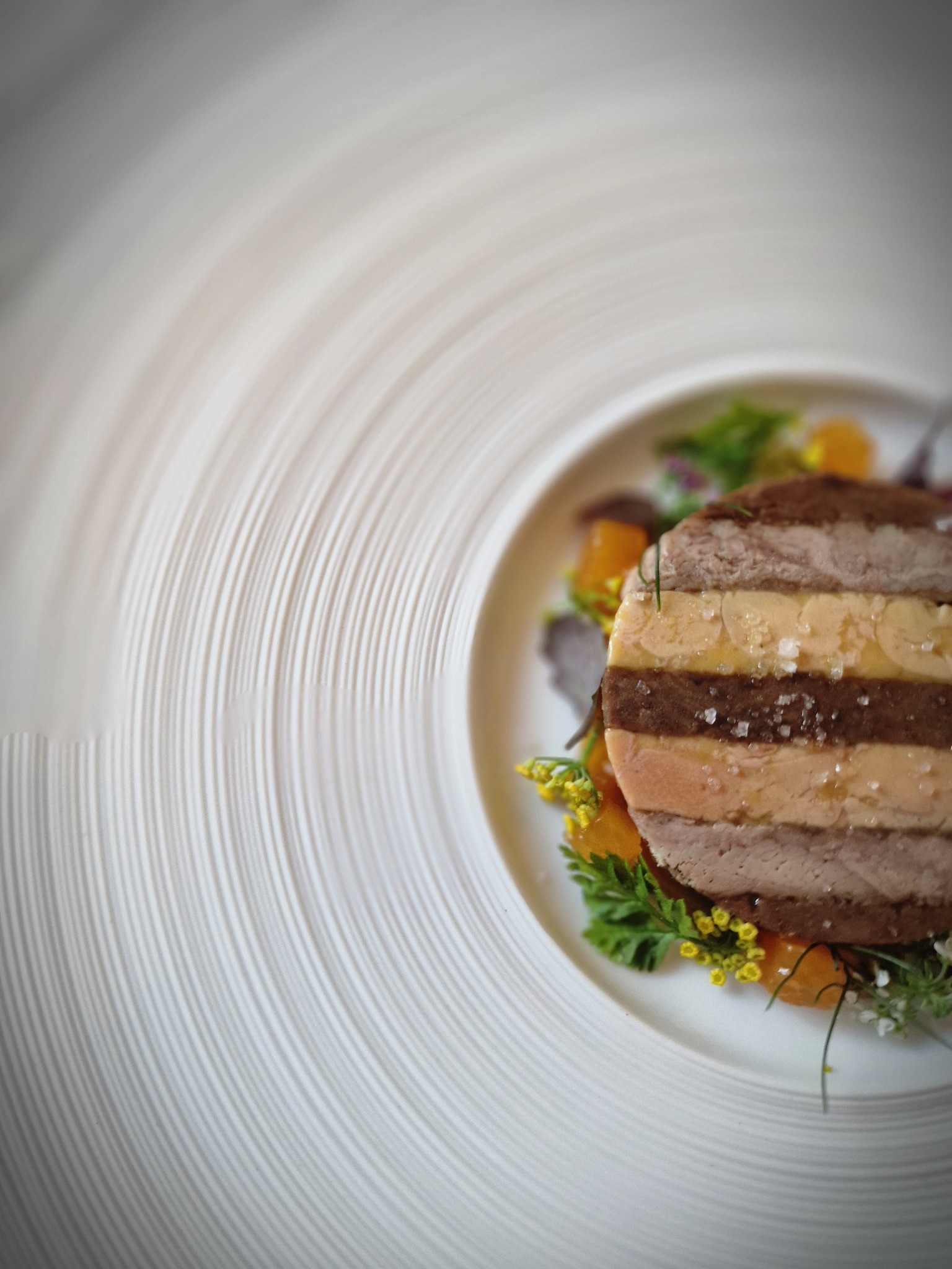 Sliced layered foie gras terrine with fruit purée, herbs and flowers on a white plate