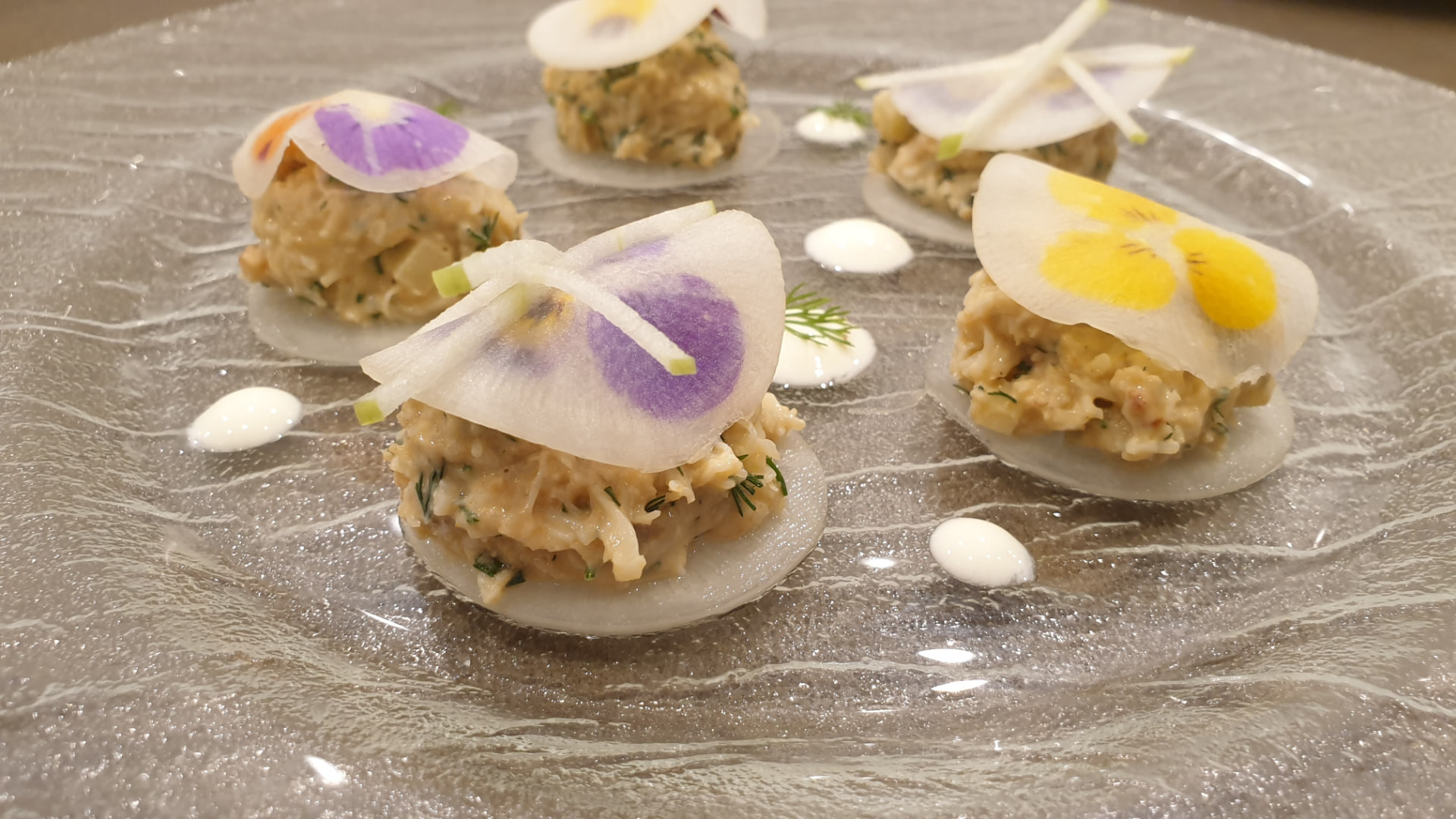 Crab and dill canapés on mooli discs with pressed pansies on a glass plate