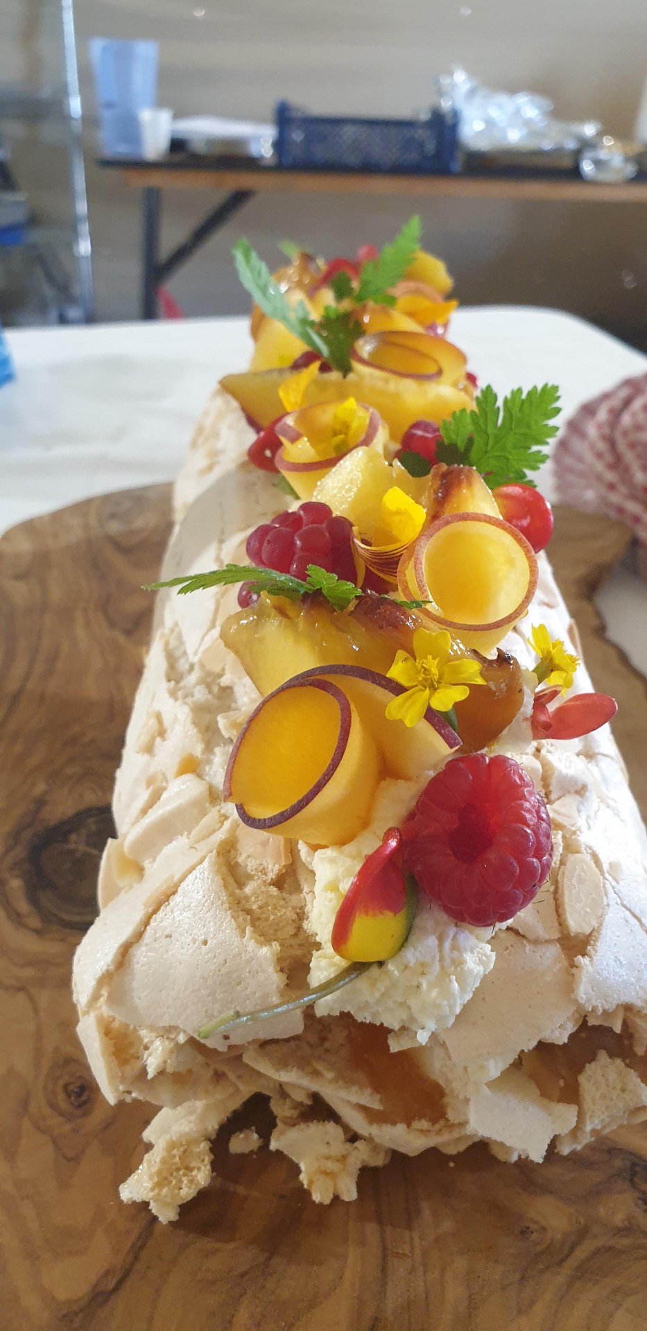 Meringue roulade topped with stone fruit and raspberries on an olive board