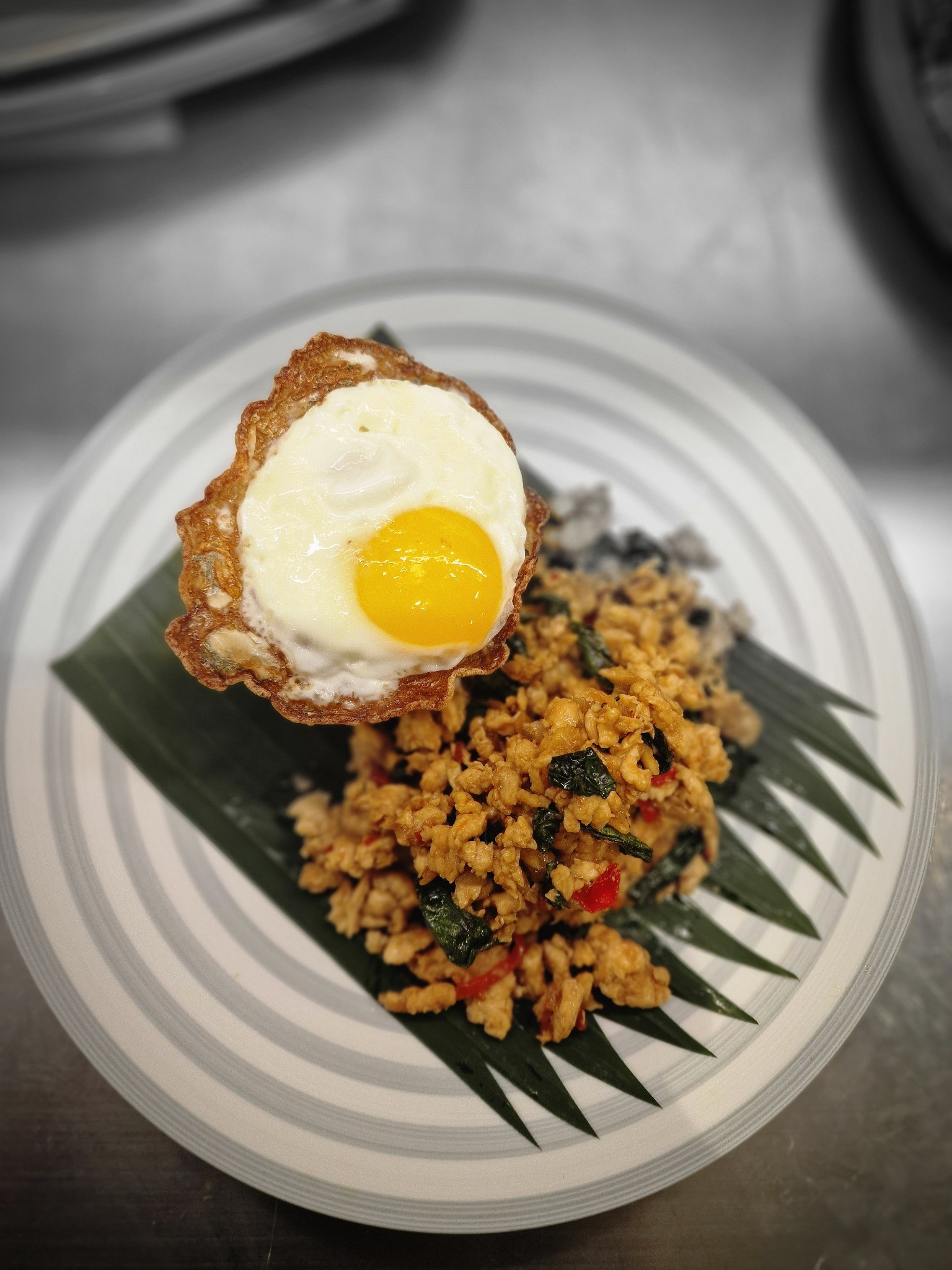 Stir-fried minced chicken with basil and a fried egg served on a banana leaf