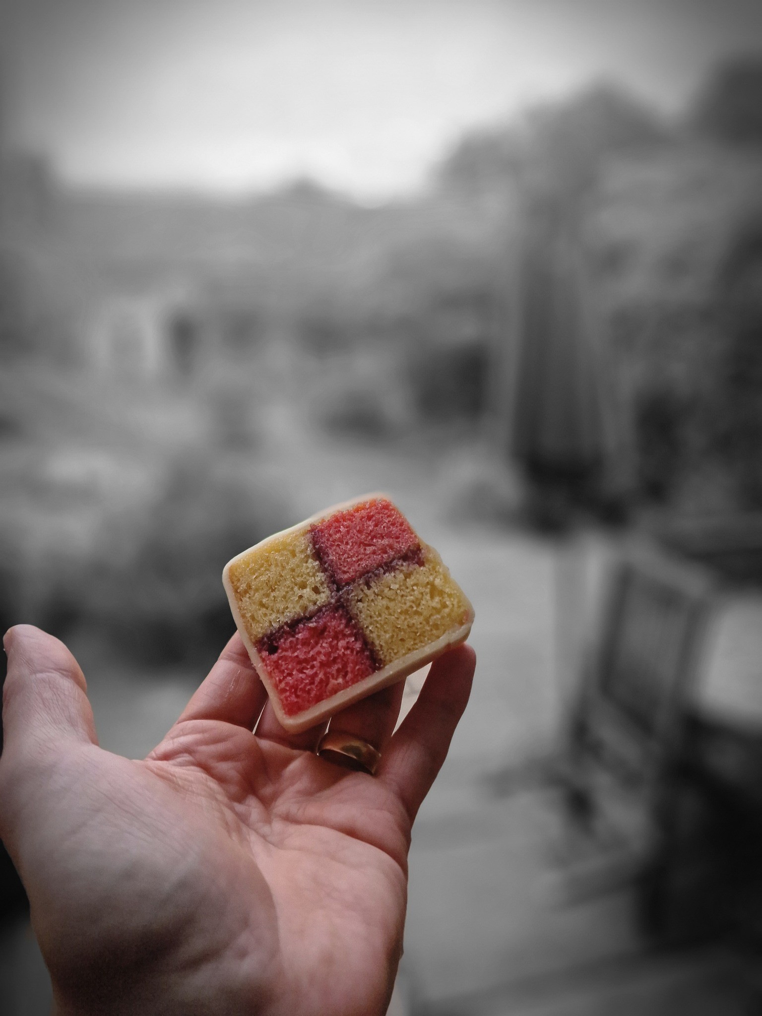 A hand holding a square of Battenberg cake with a checkered pink and yellow sponge