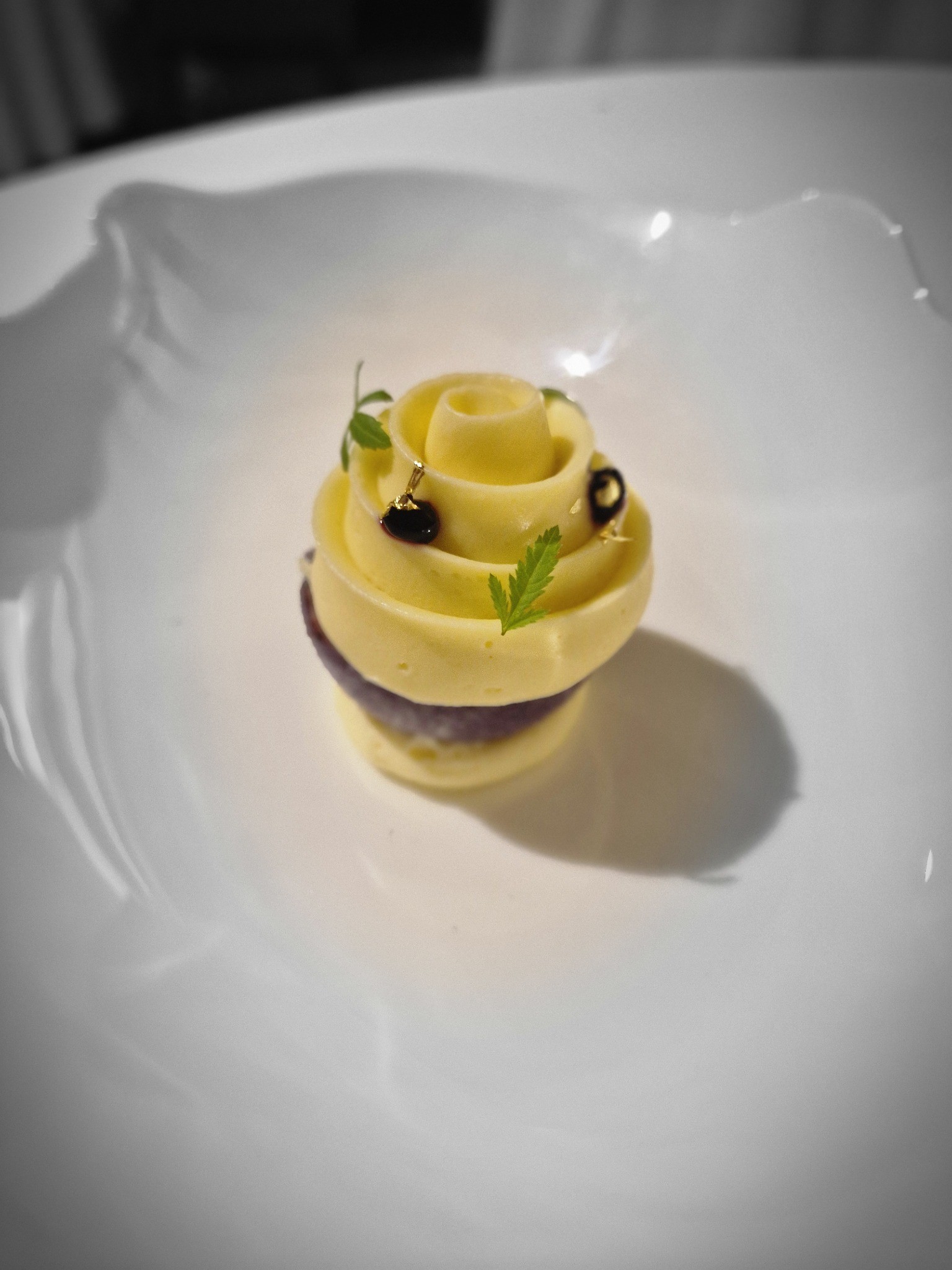 Spiral-shaped yellow dessert garnished with dark berries and green leaves
