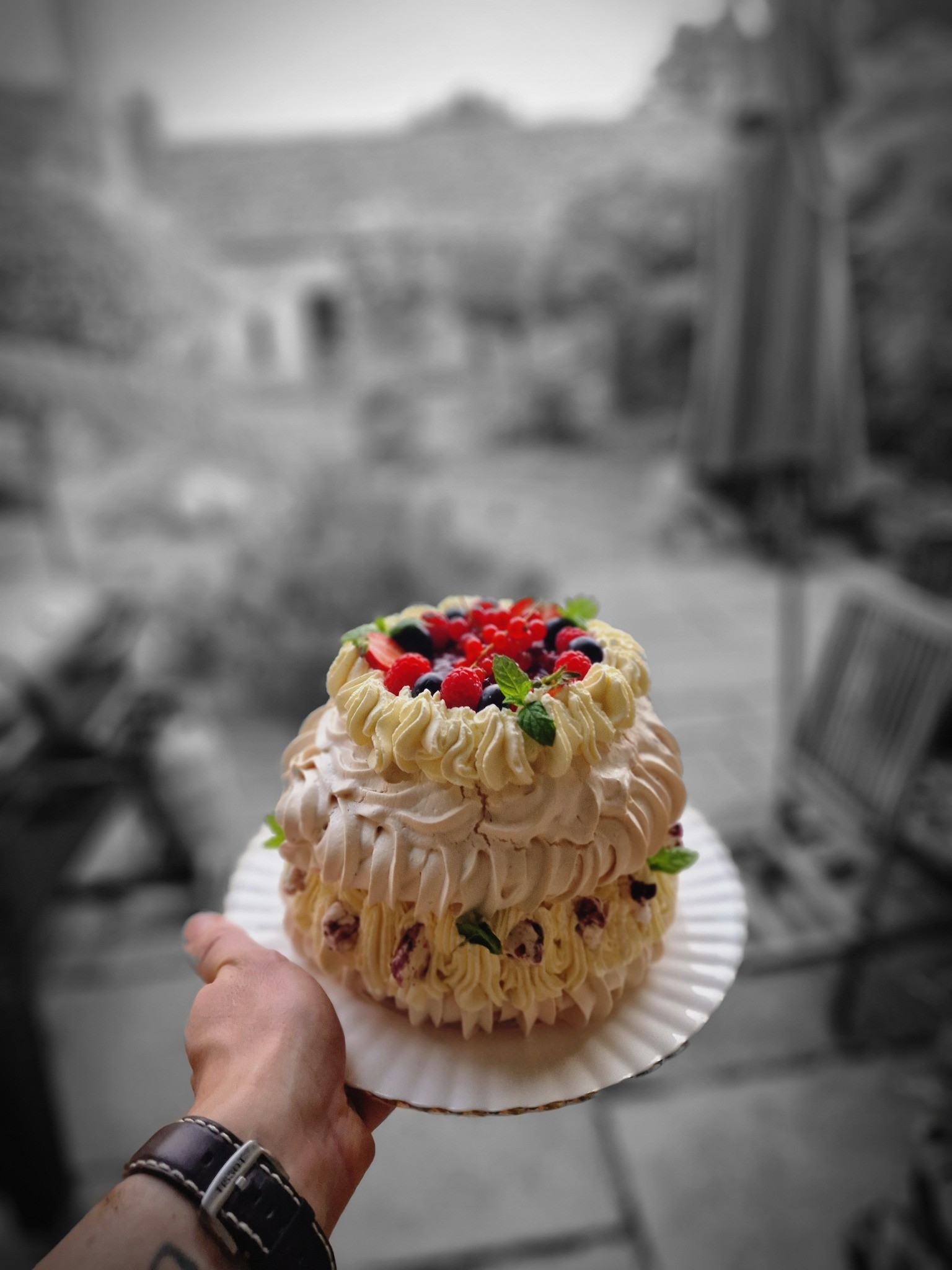 A hand holding a tiered pavlova topped with berries and mint